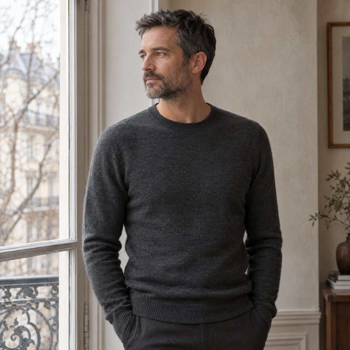 Homme en pull en laine mérinos anthracite devant une fenêtre parisienne