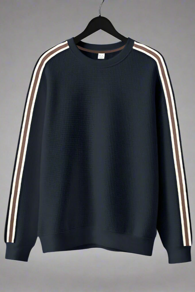Black sweatshirt with white stripes on sleeves hanging against a gray background