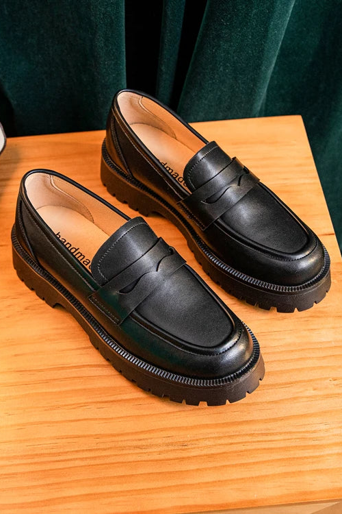 Pair of black loafers on a wooden surface with a dark green curtain background