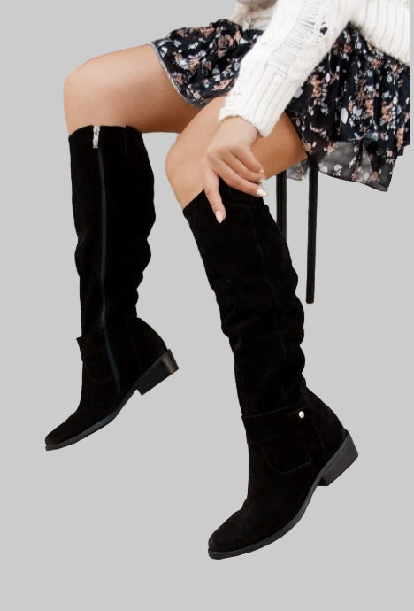 Black knee-high boots worn by a person on a gray background