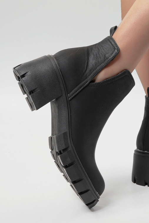 Black Chelsea boots worn by a person on a light gray background