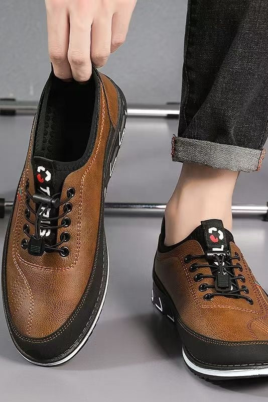 Brown leather shoes with black accents worn by a person on a gray floor.