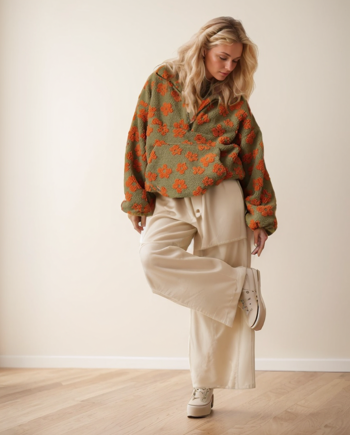 Woman wearing a green floral sweater with beige pants and white sneakers in a minimal indoor setting.