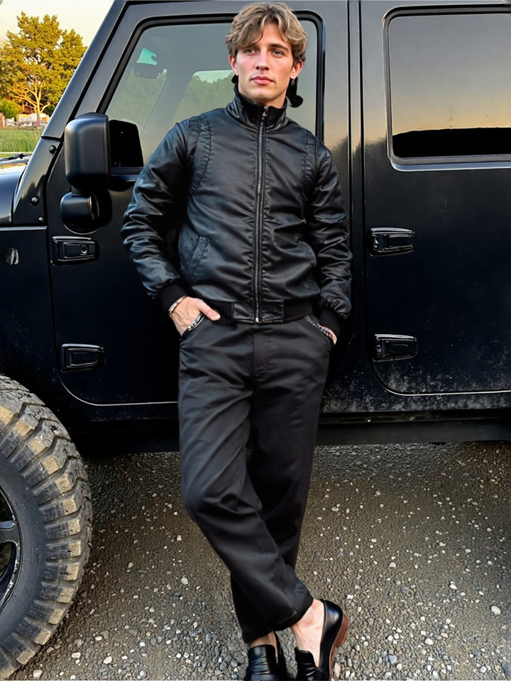 Man in a black jacket and pants standing next to a black vehicle.