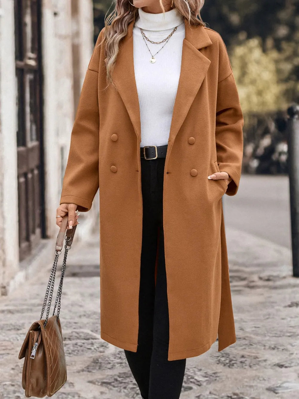 A woman wearing a caramel coat  with a beown bag in hand 
