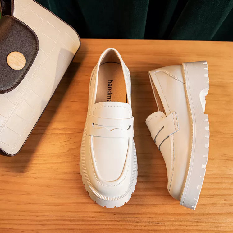 Pair of cream-colored loafers on a wooden surface with a small bag.