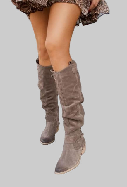 Brown suede knee-high boots worn by a person on a gray background