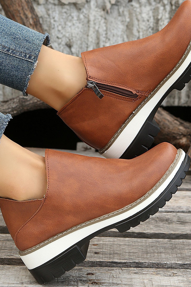 Brown leather boots with white soles worn by a person on a wooden surface