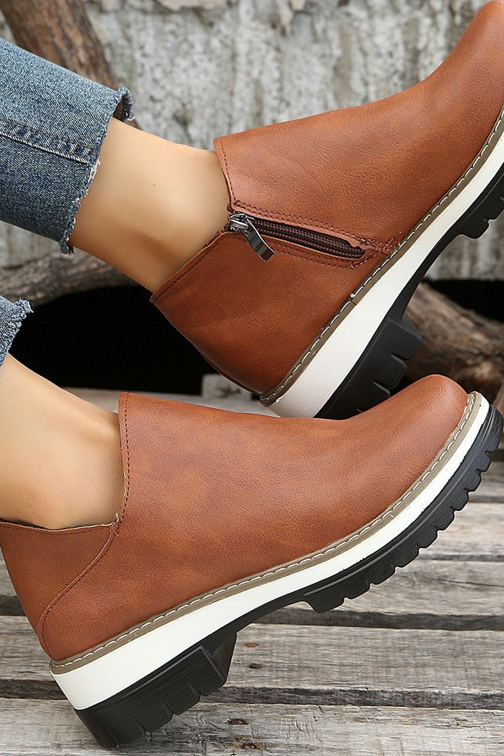 Brown leather boots with white soles worn by a person on a wooden surface