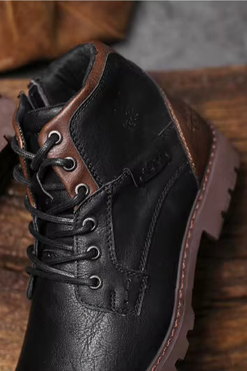 Pair of black leather shoes with brown soles on a wooden surface