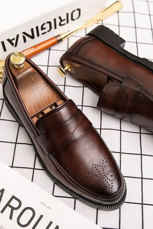 Brown leather loafers on a grid background with a pen and paper.