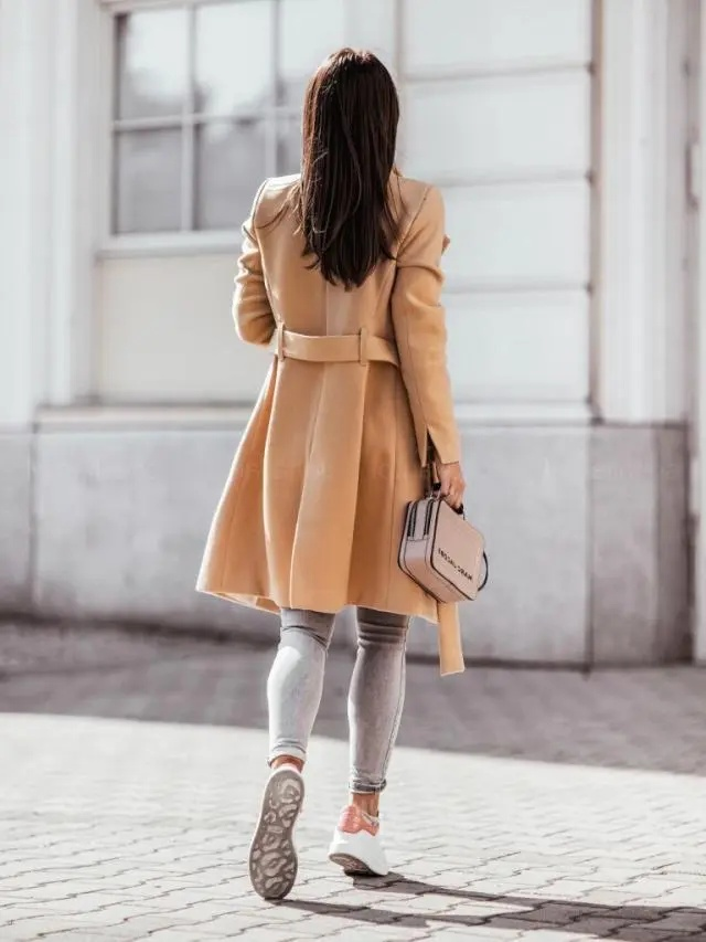Woman wearing a beige coat walking on a street.