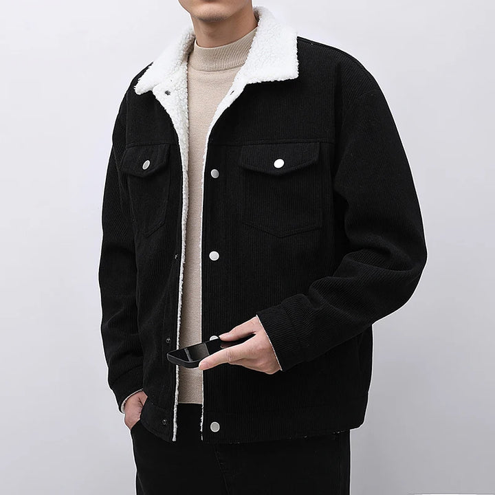 Person wearing a black jacket with white fleece lining on a plain background