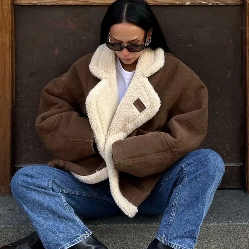Person wearing a brown shearling coat sitting against a wall.