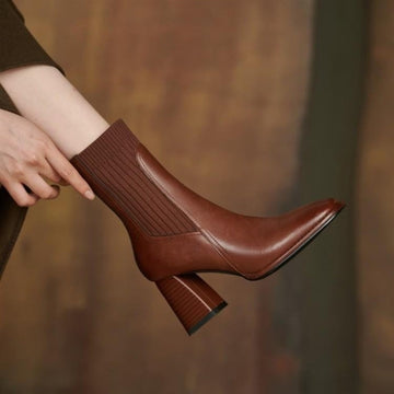 Brown leather boot with a block heel held by a person against a blurred background